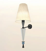 A modern wall sconce light fixture featuring a tapered beige pleated fabric shade, a matte black wall mount and arm, a white glass cone shade, and a small light blue decorative bead accent near the bottom.