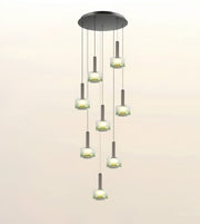 A modern multi-light chandelier pendant fixture with a circular dark metal canopy, multiple hanging cords, and cylindrical frosted glass shades glowing with warm light, shown against a plain light background.