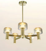 A modern five-light chandelier with a brushed gold/brass metal frame and clear glass cylindrical shades, shown against a plain off-white background.