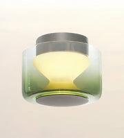 A modern flush-mount ceiling light fixture with a translucent green-to-clear gradient glass shade, a gray top canopy, and a warm yellow illuminated diffuser, shown against a plain off-white background.