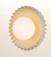A modern circular wall sconce with a fluted, scalloped outer rim in a warm beige tone and a smooth, frosted white central globe, shown against a plain off-white background.