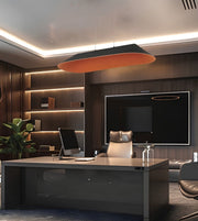 A modern office interior with a large dark desk, office chair, built-in shelving with warm LED lighting, a wall-mounted screen, and a distinctive oval pendant light with a black exterior and orange interior hanging above the desk.
