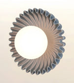 A modern circular pendant light with a wide, fluted scalloped rim and a central glowing white globe shade, shown against a plain off-white background.