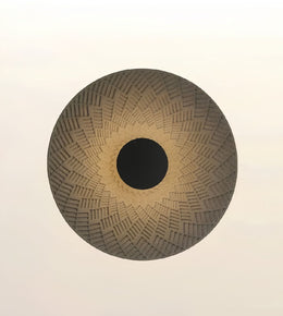 A circular woven basket or mat with a textured geometric pattern, featuring a dark brown center and a light brown outer rim, set against a plain off-white background.