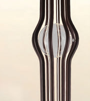 A close-up of a modern sculptural glass object with multiple dark brown vertical tubes framing a clear oval glass center, set against a warm cream background.