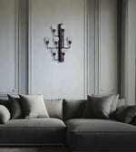 A modern multi-arm wall sconce with frosted glass globes mounted on a light gray paneled wall above a dark gray sectional sofa with matching pillows.