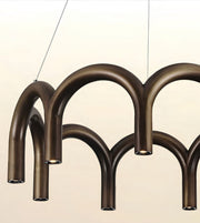 A modern multi-arm chandelier with a dark bronze metallic finish, suspended by thin cables against a light beige background.