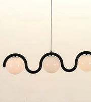 A modern three-light linear pendant chandelier with a black wavy metal frame and frosted white glass globes, suspended against a plain off-white background.