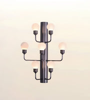 A modern multi-light wall sconce with a matte black central column and six curved arms, each holding a glowing frosted globe bulb, shown against a plain light background.