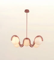 A modern wavy pendant light fixture with a dusty rose metal frame and five frosted glass globes, suspended from a matching ceiling canopy against a soft off-white background.