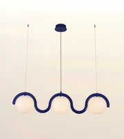 A modern three-light linear pendant chandelier with a wavy, S-shaped dark blue frame and three frosted white globe shades, suspended from a matching dark blue ceiling canopy.