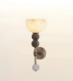 A wall-mounted sconce with a frosted glass dome shade, two dark textured spherical accents, a brass-toned vertical stem, and a round white glass finial, shown against a soft off-white background.