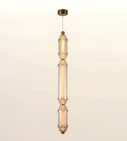 A modern vertical pendant light fixture with three stacked cylindrical glass shades in a warm frosted amber tone, accented by brass-toned metal hardware and a matching ceiling canopy, shown against a plain off-white background.