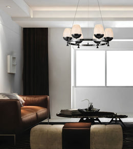 Modern multi-light chandelier with five tapered beige shades and black metal arms, suspended in a contemporary living room with a brown leather sofa and dark window treatments.
