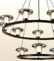 Modern multi-tier ring chandelier with brushed silver metal circular frames, black suspension rods, and glowing warm white glass shades.
