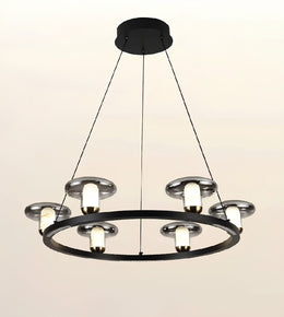 A modern multi-light ring chandelier with a matte black circular frame, silver-toned metal shades, and glowing warm white bulbs, suspended by thin black cords from a round ceiling canopy against a plain light background.