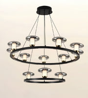 A modern multi-light chandelier with a black metal frame in two concentric rings, featuring multiple circular glass shades and warm white light bulbs, shown against a plain off-white background.