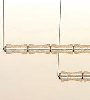 A modern multi-light linear chandelier with textured, translucent glass cylindrical shades suspended by thin black wires against a warm cream background.