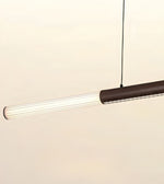 A modern linear pendant light with a ribbed clear glass shade and a dark brown metal body, suspended by a thin black cord against a plain off-white background.