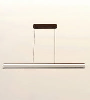 A modern linear LED pendant light with a slim silver-white bar, suspended by two thin cables from a dark brown rectangular ceiling mount against a plain off-white background.