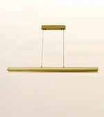 A modern linear LED pendant light fixture in a brushed gold finish, suspended by two thin black cables from a matching rectangular ceiling canopy, shown against a plain off-white background.
