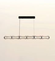 A modern linear chandelier with five textured, translucent glass cylindrical shades suspended from a black rectangular ceiling canopy against a warm off-white background.