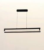 A modern linear LED pendant light fixture in black, suspended by two thin cables from a rectangular ceiling mount against a plain off-white background.