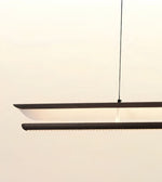 A modern linear LED pendant light with a matte black frame and a warm white glowing diffuser, suspended by a thin black cord against a plain off-white wall.