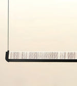A modern linear pendant light suspended by a thin black cord, featuring a black frame and a textured white and gray striped diffuser panel.