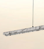 A modern linear pendant light with a white and gray marble-patterned outer shell and a silver metal frame, suspended by a thin black cord against a warm off-white background.