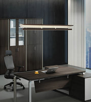 A modern office setup featuring a dark wood executive desk with a matching dark wood hutch, a black office chair, and a sleek rectangular pendant light hanging above the desk.