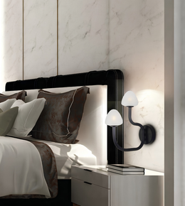 A modern black wall sconce with two curved arms and white dome-shaped shades, mounted on a light marble wall next to a bed with white and brown bedding.