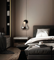A modern wall-mounted glass pendant light with a black wall mount and a warm glowing bulb, hanging on a taupe wall in a contemporary bedroom setting.