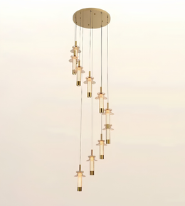 A modern multi-light linear pendant chandelier with a circular brushed brass ceiling canopy, slim hanging cords, and multiple cascading glass shades with brass accents, shown against a plain light background.