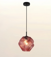 A modern pendant light with a textured, ribbed glass shade in a dusty rose or terracotta pink color, suspended by a slim black cord from a matching black ceiling canopy against a light beige background.