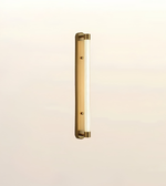 A modern vertical linear wall light fixture with a brushed brass or gold finish and a frosted glass tube, shown against a plain off-white background.
