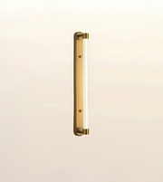 A modern vertical linear wall light fixture with a brushed brass or gold finish and a frosted glass tube, shown against a plain off-white background.
