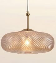 A modern pendant light with a textured, diamond-patterned glass shade in a warm champagne or blush tone, suspended by a brass-colored rod against a plain off-white background.