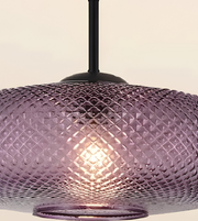 A close-up of a hanging pendant light with a textured, diamond-patterned purple glass shade and a black ceiling canopy.