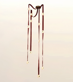 A hanging decorative wind chime with dark reddish-brown ribbons and cream circular beads, suspended from a dark metal fixture against a plain light background.