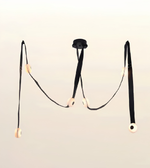 A modern black chandelier with three long hanging straps and circular cream-colored light diffusers, suspended against a plain off-white background.