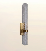 A modern wall sconce featuring a textured, cylindrical frosted glass shade with a brushed gold metal bracket and band.