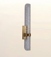 A modern wall sconce featuring a textured, cylindrical frosted glass shade with a brushed gold metal bracket and band.