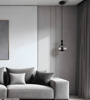 A modern living room scene featuring a light gray fabric sofa with dark gray and white throw pillows, a dark gray wall with vertical paneling, a black pendant light with a metallic silver globe shade, and a dark gray curtain.