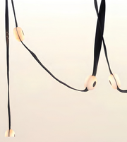 A minimalist black cord pendant light with smooth, rounded off-white wooden beads spaced along the cord, photographed against a clean, light off-white background.