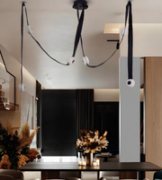 Modern multi-light pendant chandelier with black fabric cords, white circular diffusers, and spherical globe shades, shown hanging in a contemporary interior space.