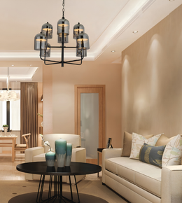 A modern multi-light chandelier with smoky glass shades and black metal arms hangs in a contemporary living room with beige walls, a cream sofa, and a round black coffee table.