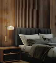 A modern bedroom scene featuring a dark upholstered bed with white and gray pillows, a matching dark headboard, a warm wood slat accent wall, a lit wall sconce, and a wooden nightstand.