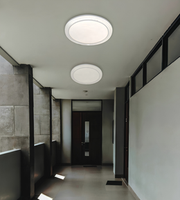 Two round flush-mount ceiling light fixtures installed on a white ceiling in a modern hallway with gray tiled walls and a dark wooden door.