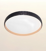 A modern flush-mount ceiling light with a textured black outer ring, a frosted white diffuser, and a warm beige inner trim, shown against a plain beige background.